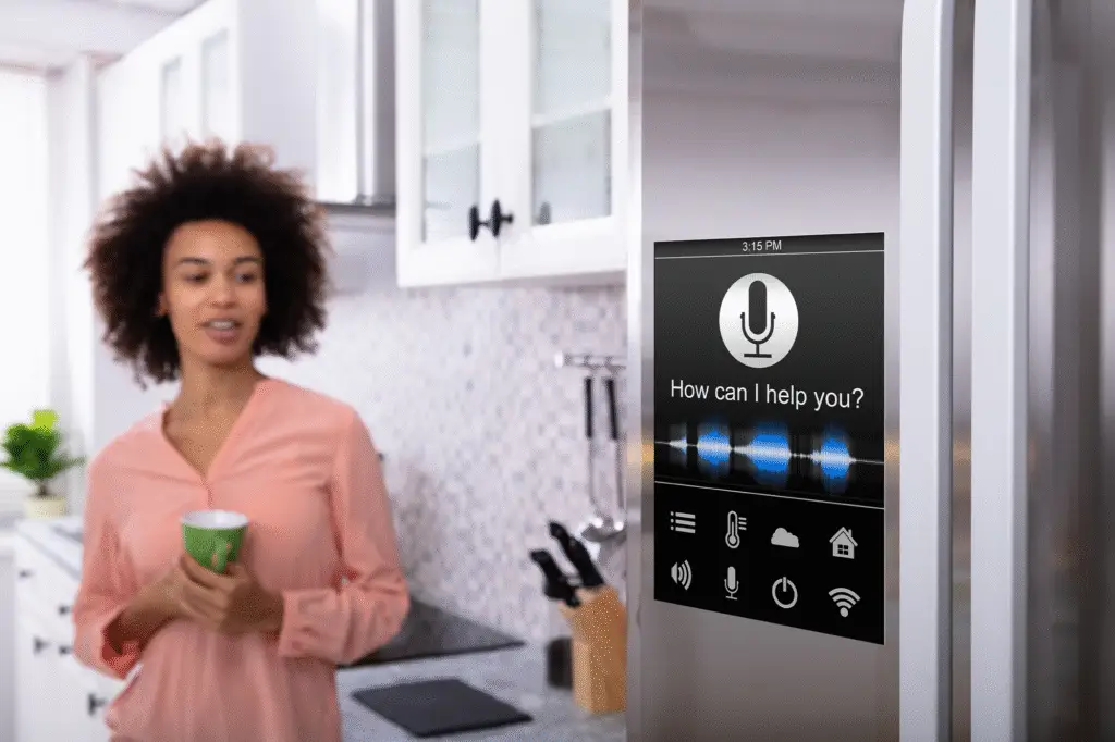A woman standing in her kitchen. smiling while looking at a "smart" refrigerator
