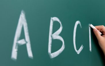 A picture of a hand holding a piece of chalk, writing "A B C" on a chalk board