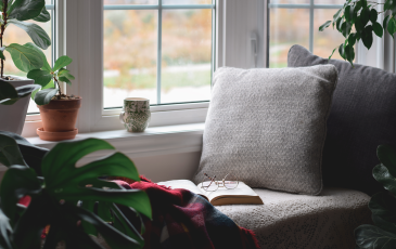 A cozy, relaxing reading area, featuring a cushy chair with a book and some glasses in the middle of it, next to a window,