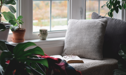 A cozy, relaxing reading area, featuring a cushy chair with a book and some glasses in the middle of it, next to a window,