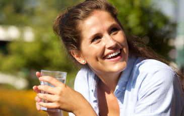 A woman smiling while holding a cold drink on a sunny summer day