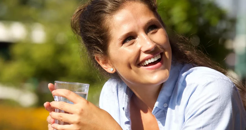 A woman smiling while holding a cold drink on a sunny summer day