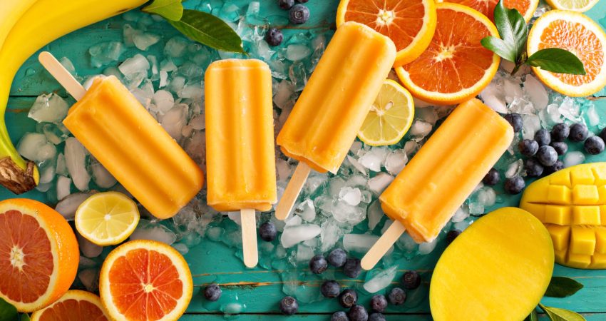 A picture of some popsicles laying on a table surrounded by ice and orange slices