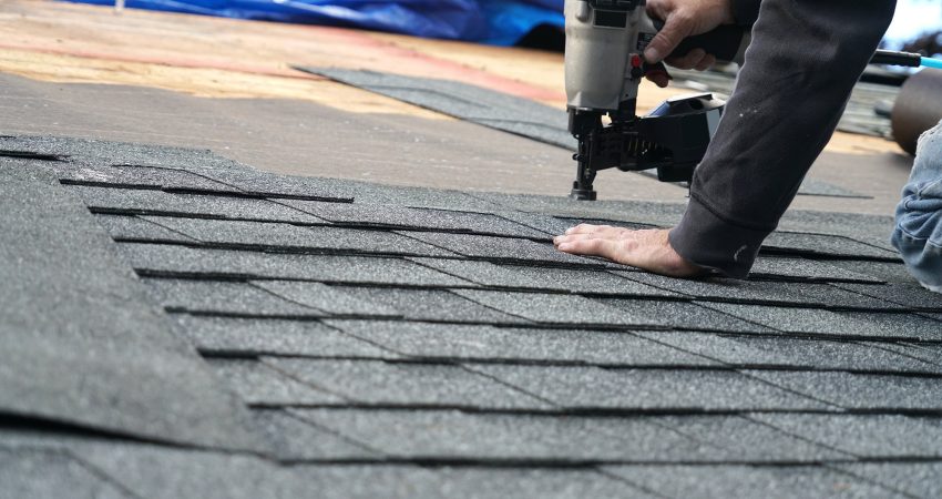 handyman using nail gun to install shingle to repair roof