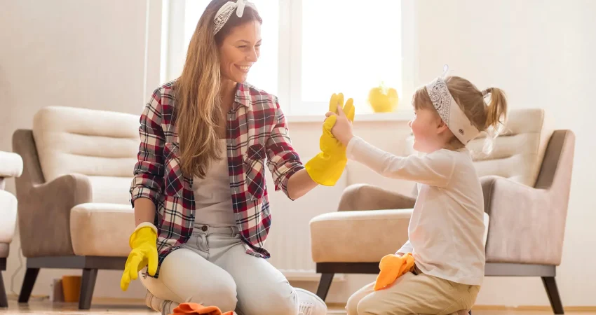 Mother and young daughter giving a high five while wearing yellow rubber gloves and cleaning the floor together at home