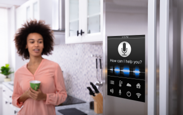 A woman standing in her kitchen. smiling while looking at a "smart" refrigerator