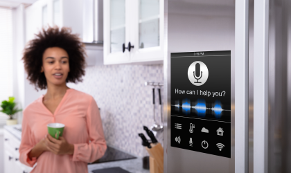 A woman standing in her kitchen. smiling while looking at a "smart" refrigerator