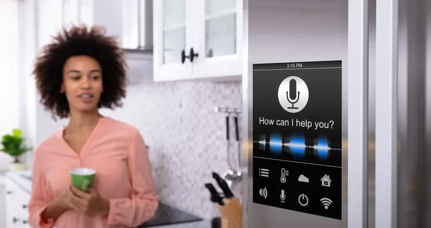 A woman standing in her kitchen. smiling while looking at a "smart" refrigerator