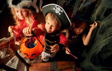 trick or treating kids Happy children in carnival costumes trick or treating with pumpkin basket in the old wooden house. Halloween party.