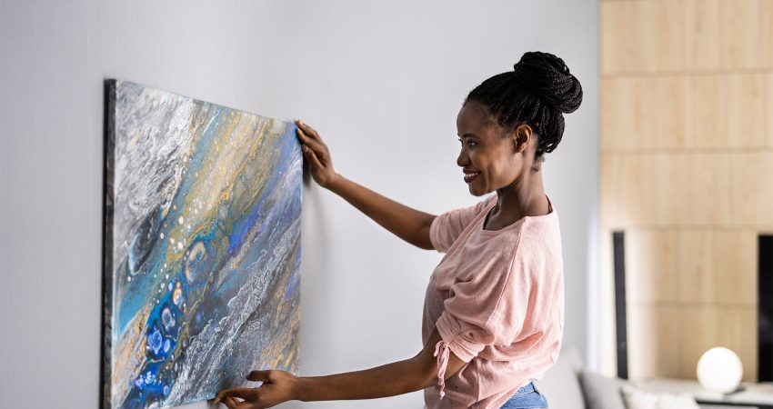 Picture of a woman hanging a painting on a wall